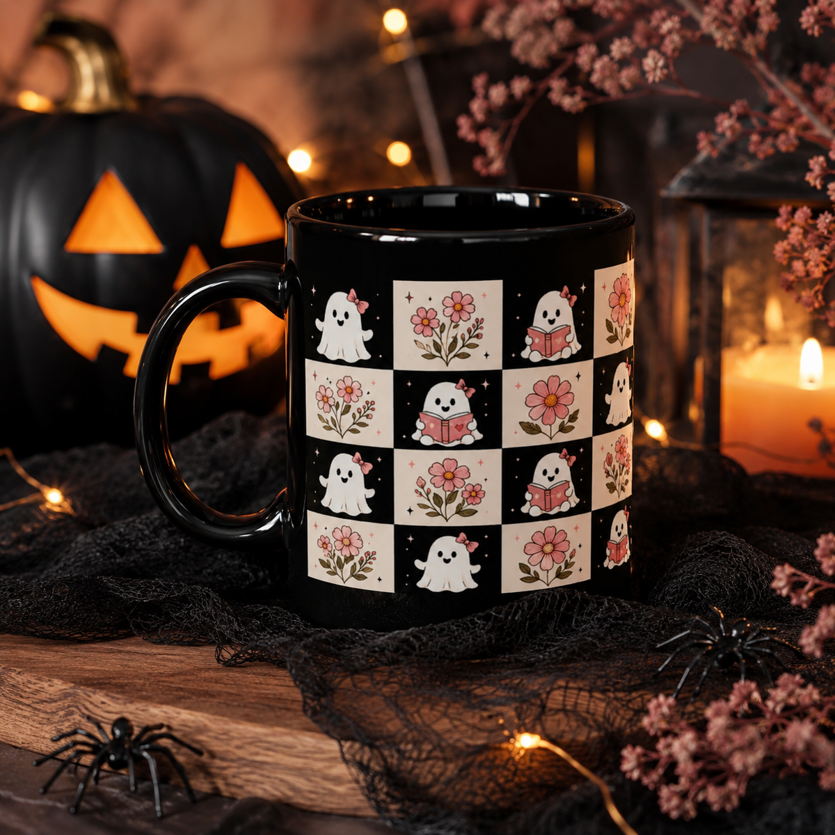 A black ceramic mug with a Halloween-themed checkerboard pattern of white ghosts and pink flowers, styled on a wooden surface with a jack-o'-lantern, candles, spider decorations, and black tinsel.