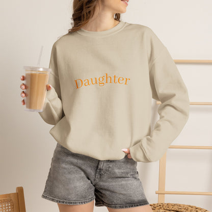 Person wearing a beige sweatshirt with a logo, holding a drink, on a neutral background